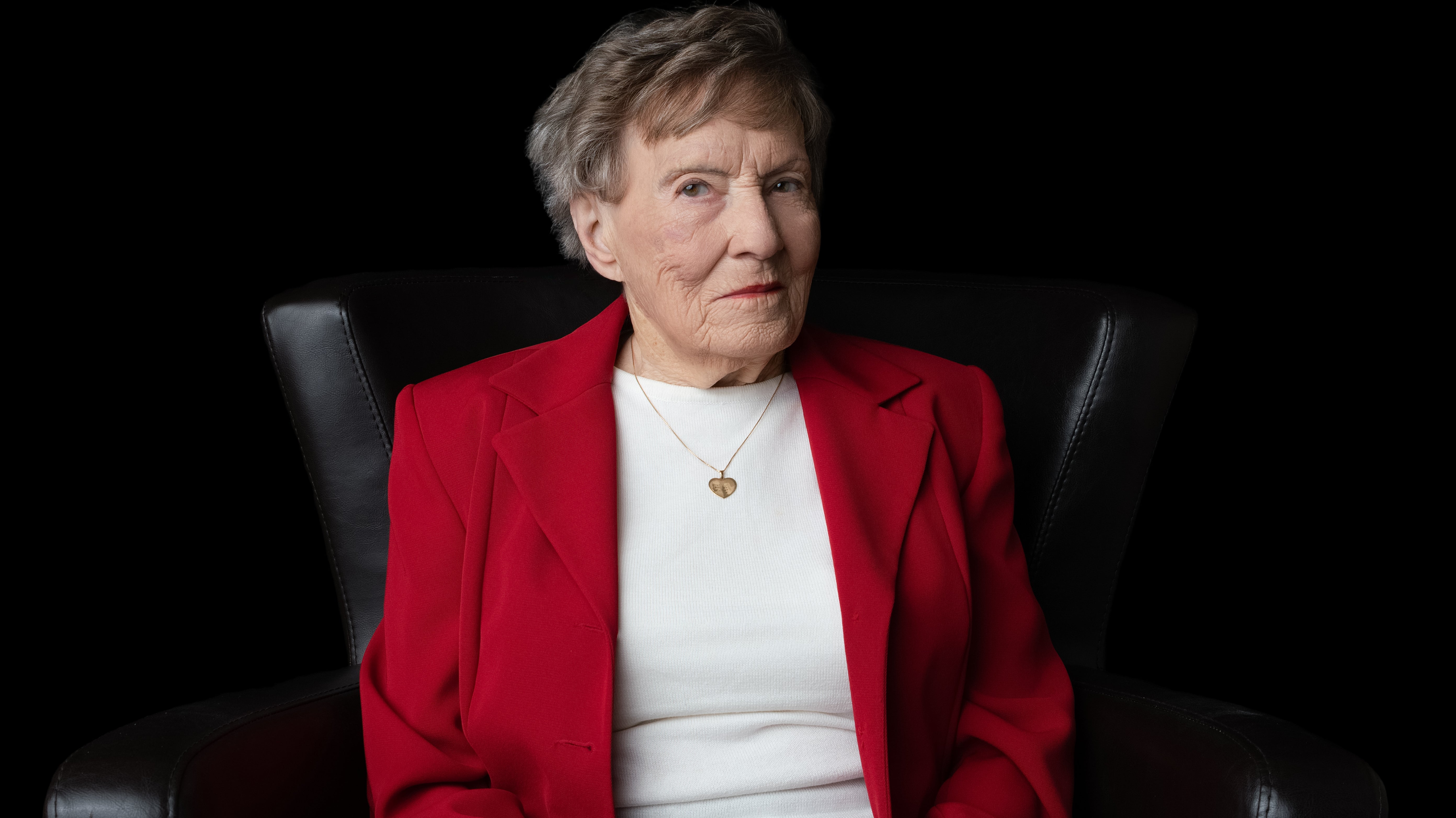 Ellen Gilchrist portrait in bright red blazer and white top against black studio backdrop, seated with dignified posture