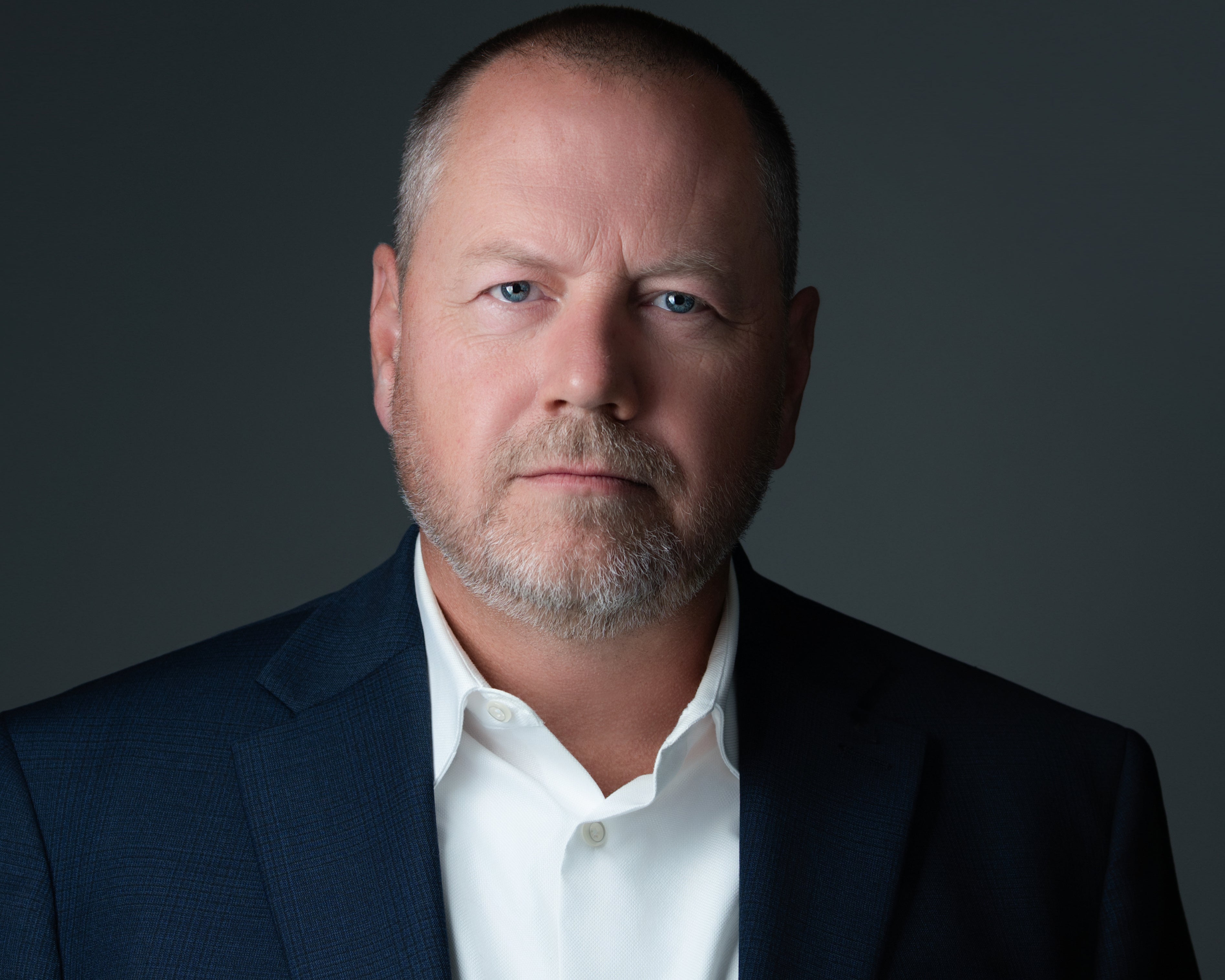 Man wearing a dark suit and white shirt against a black background