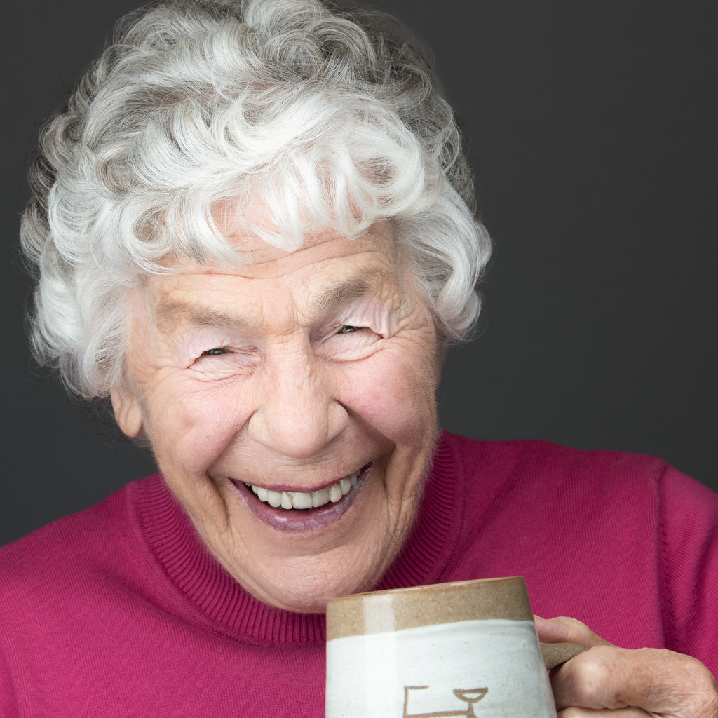 professional headshot of an elderly women, who is laughing and drinking a cup of tea