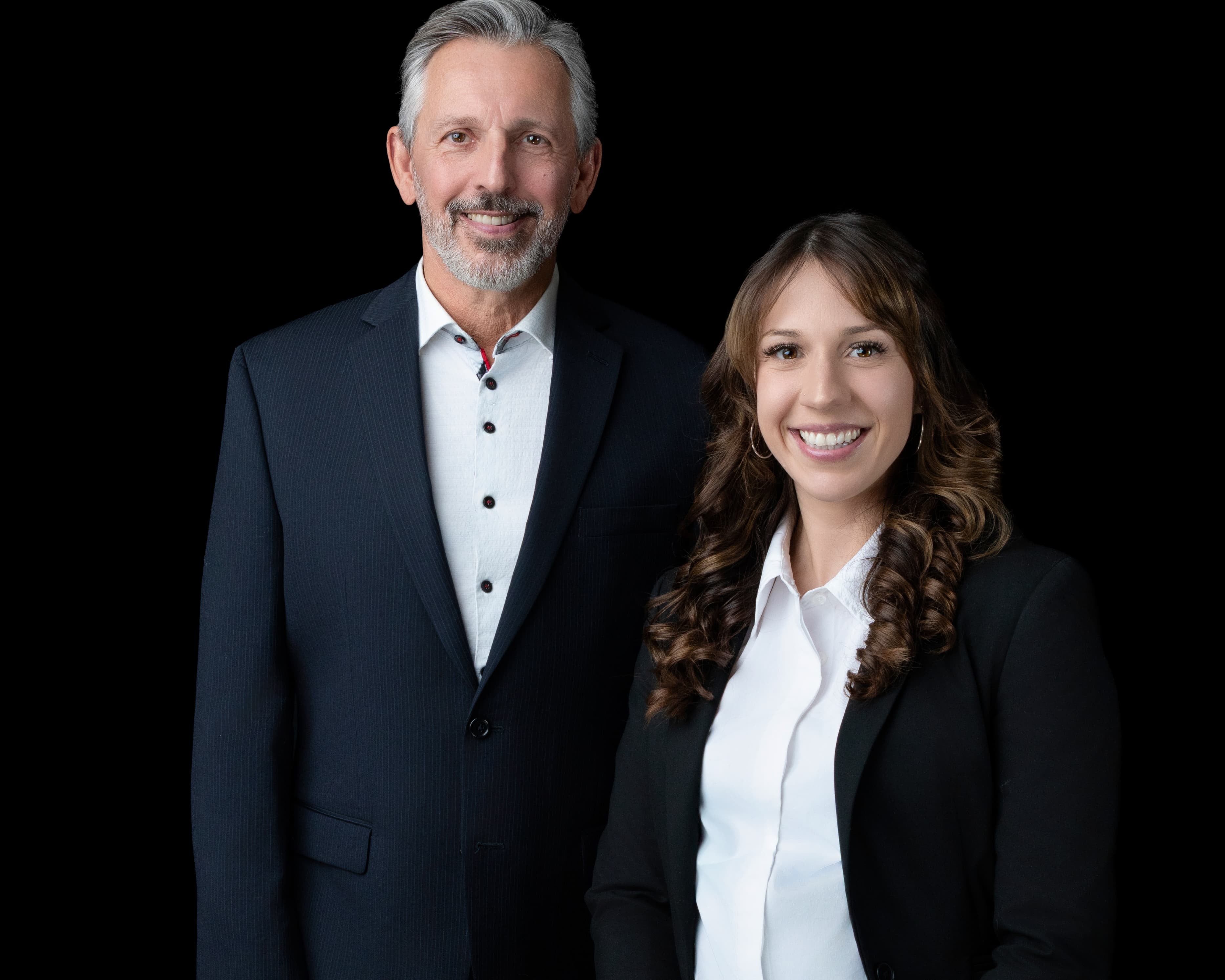 Two professionals, a man and a woman, standing side by side against a black background.