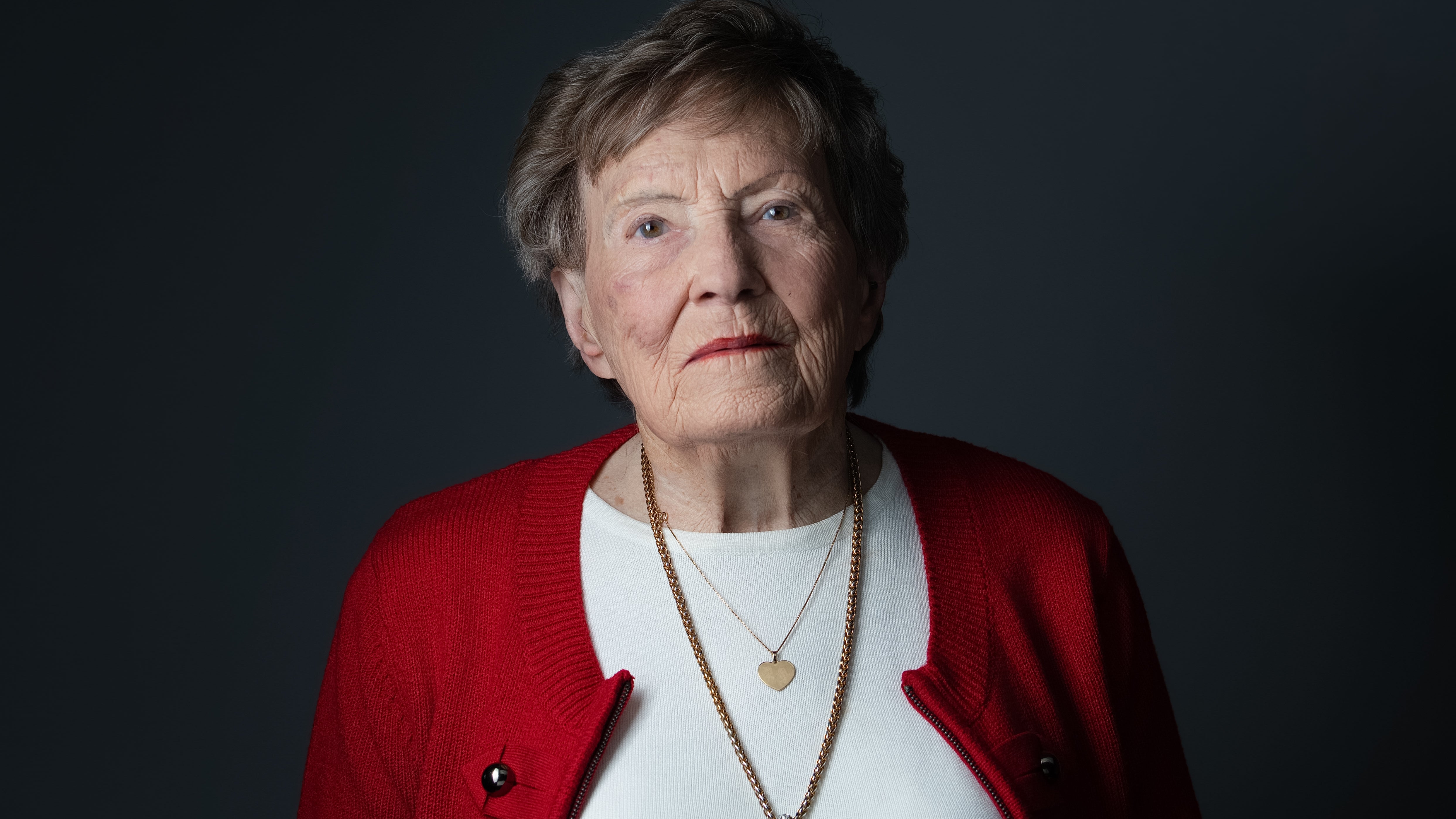 Woman wearing a red cardigan over a white shirt against a dark background