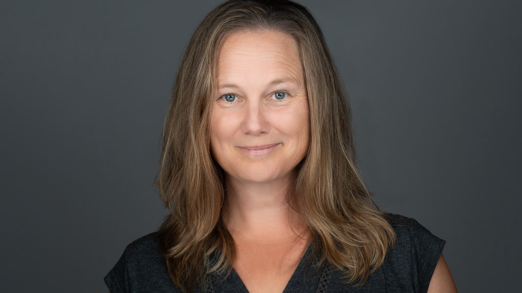 professional headshot of a smiling women, wearing a black top, on a gray background