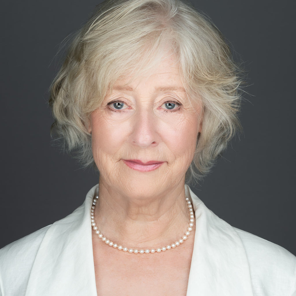 A women, who is an author, wearing a white jacket, pearl necklace, on a gray background