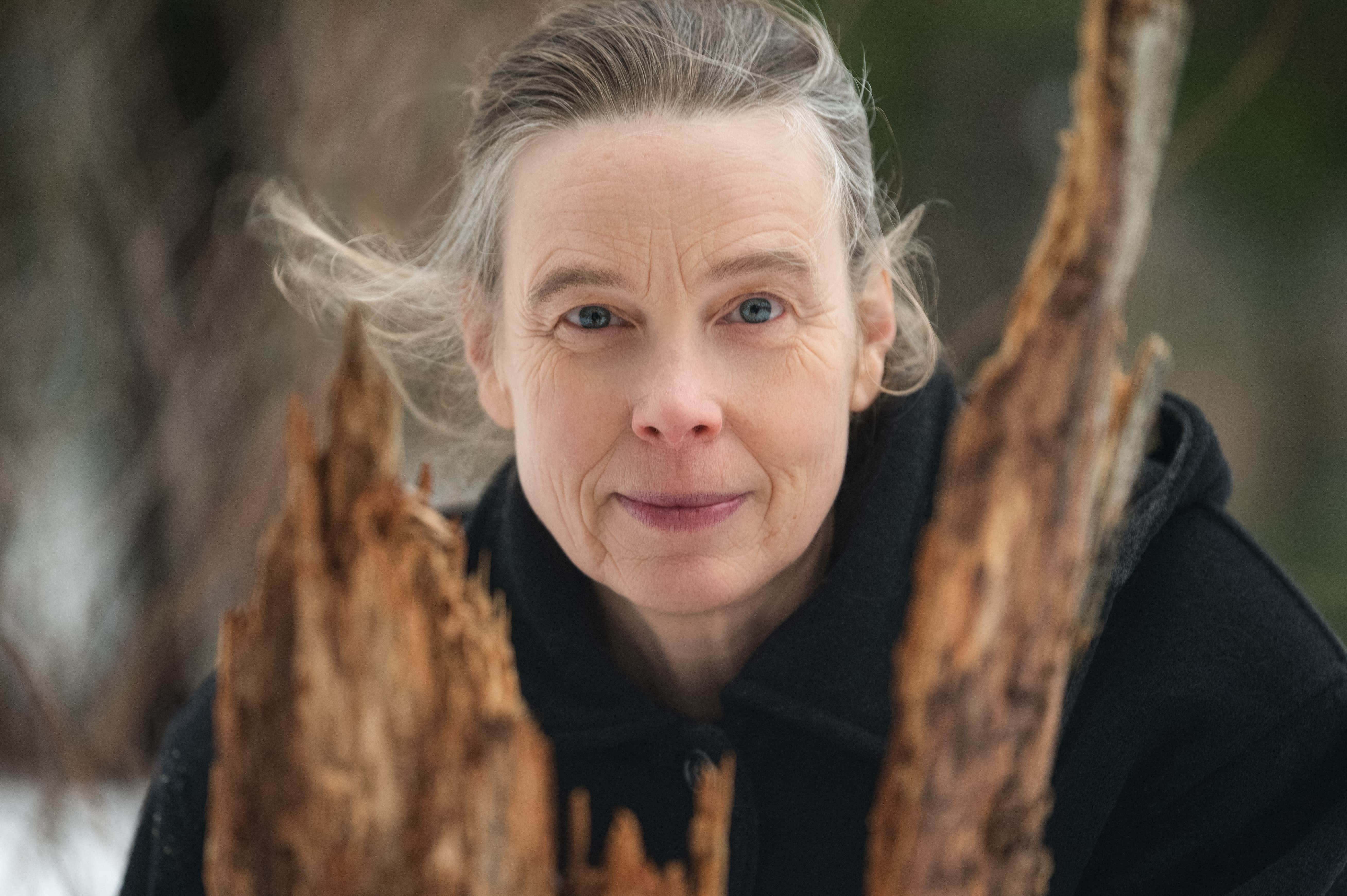 Person with gray hair standing between two large wooden logs in a natural setting