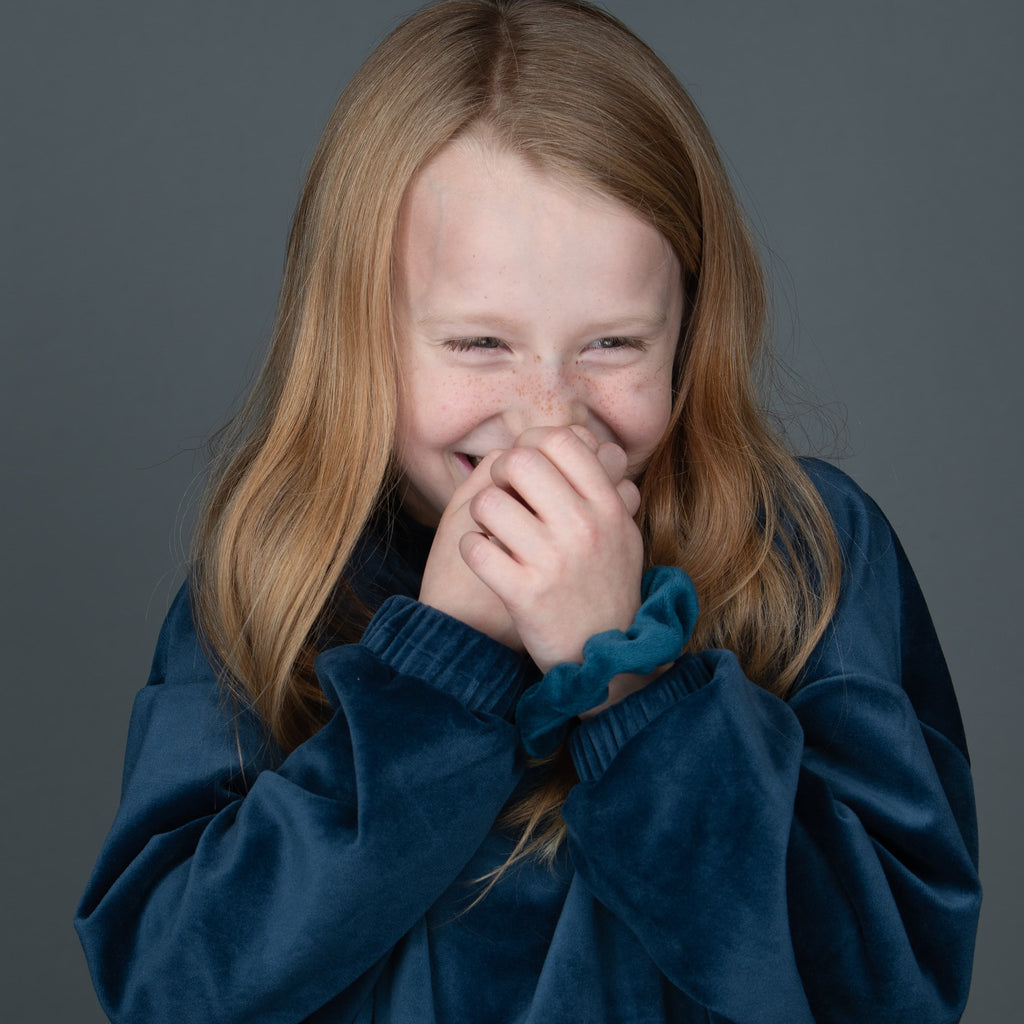 a young girl with red hair, smiling with her hands to her face, like she has a secret