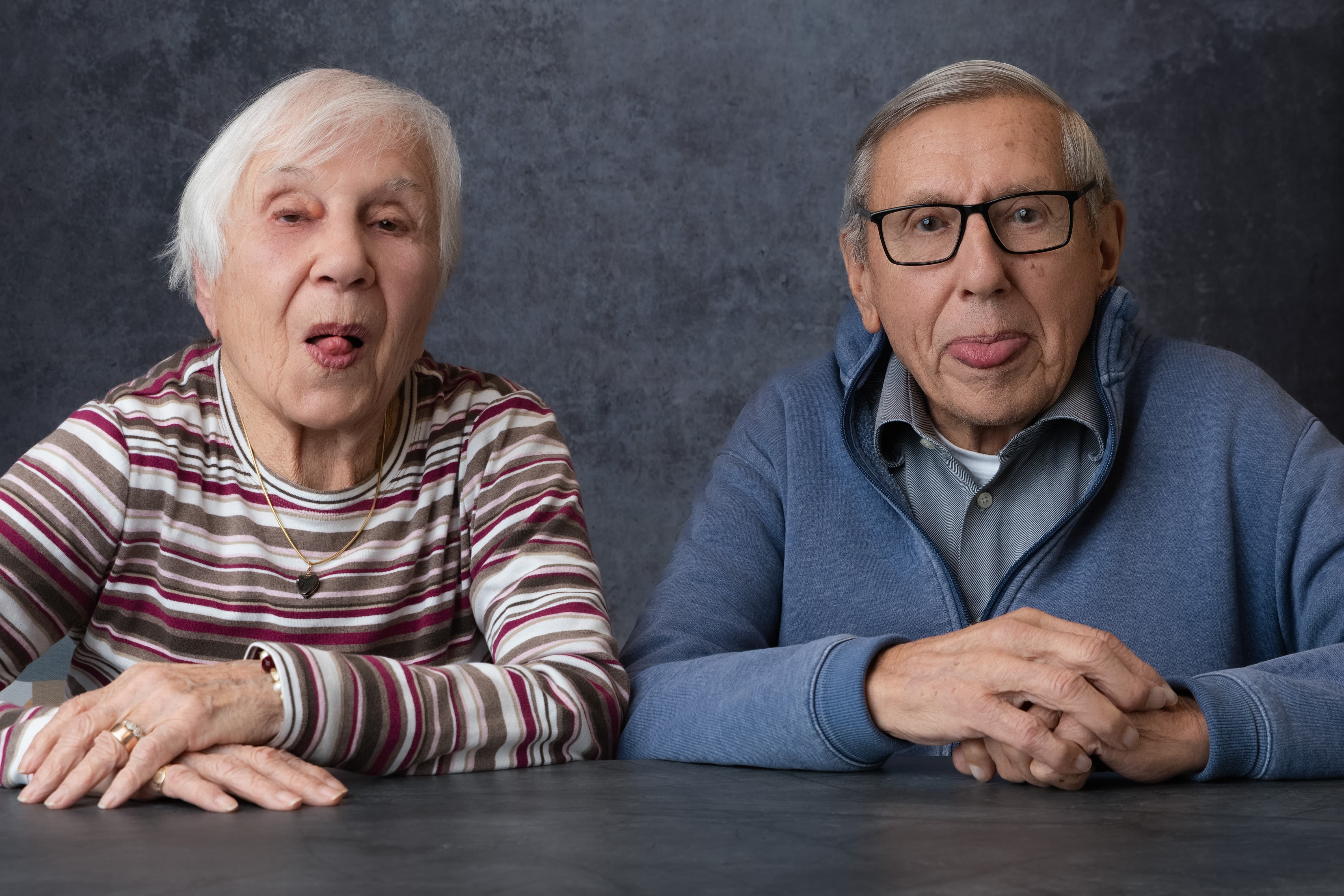 Two elderly people sitting at a table with a dark background
