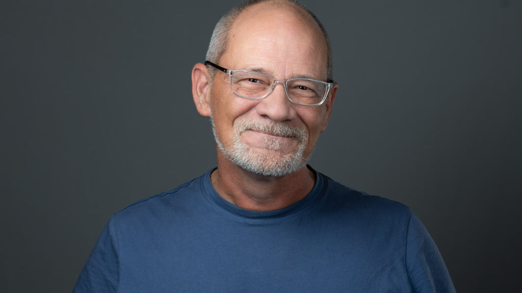 professional headshot of a man, with glasses, a beard, wearing a blue shirt, on a gray background