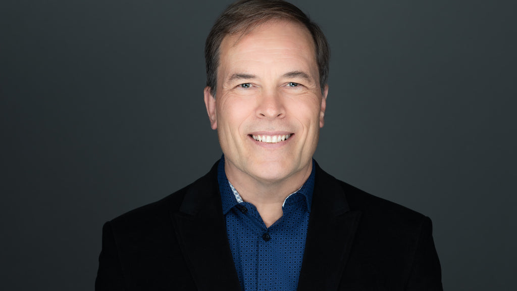 corporate headshot of a man who is wearing a blue shirt and a black jacket