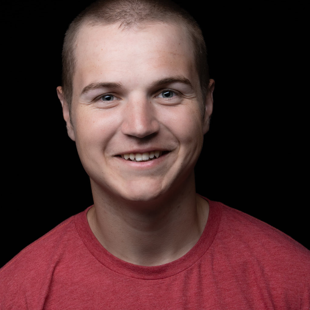 professional headshot of a young man with very short hair, wear a red t-shirts, on black background